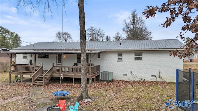 rear view of property with cooling unit, a deck, and a trampoline