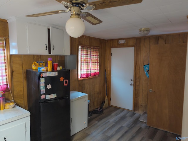 kitchen featuring white cabinetry, fridge, black fridge, and wooden walls