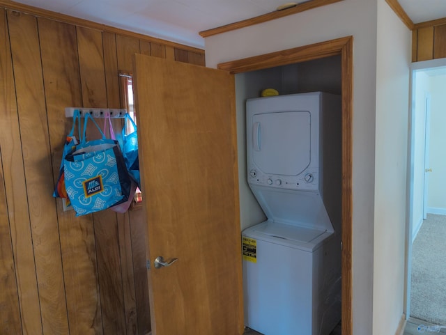 laundry area with stacked washer / dryer, carpet, and wooden walls