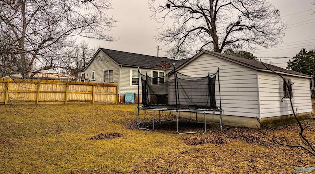 rear view of property with a trampoline and a lawn