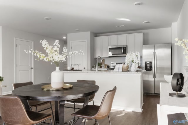 kitchen featuring appliances with stainless steel finishes, light stone counters, a kitchen island with sink, dark hardwood / wood-style floors, and white cabinetry