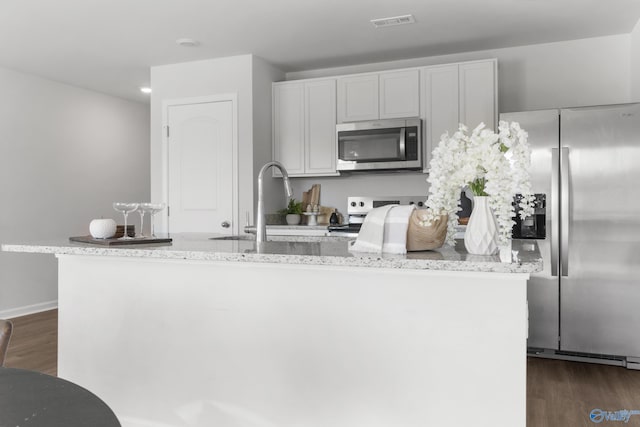 kitchen featuring light stone counters, dark hardwood / wood-style floors, a center island with sink, white cabinets, and appliances with stainless steel finishes