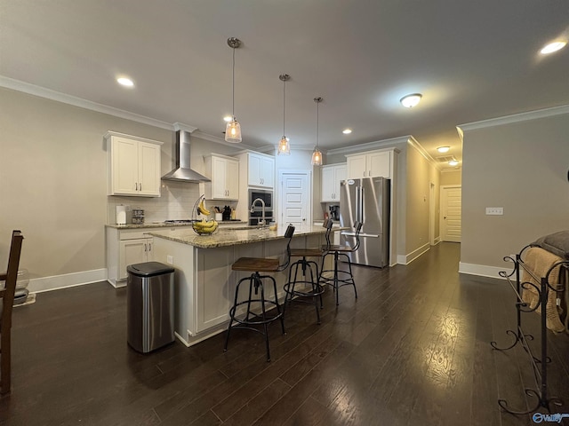 kitchen featuring a kitchen island with sink, hanging light fixtures, stainless steel appliances, white cabinets, and wall chimney exhaust hood