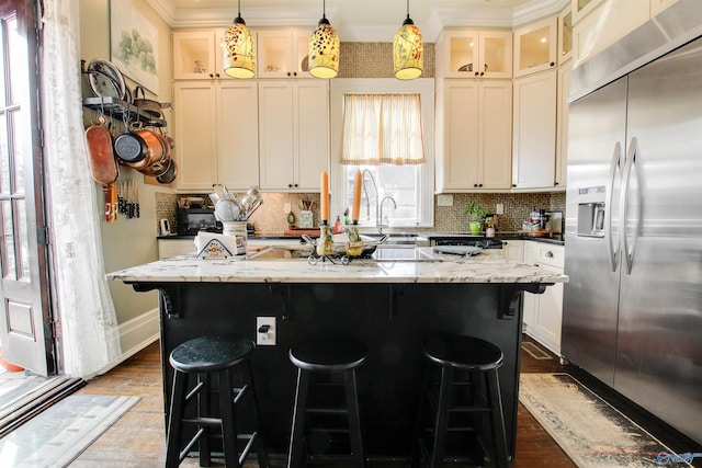 kitchen featuring an island with sink, stainless steel built in fridge, dark wood-style floors, and decorative backsplash