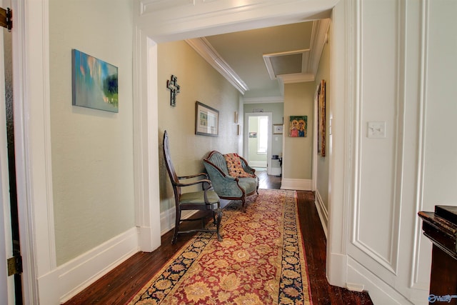 hall with dark wood-style floors, ornamental molding, attic access, and baseboards