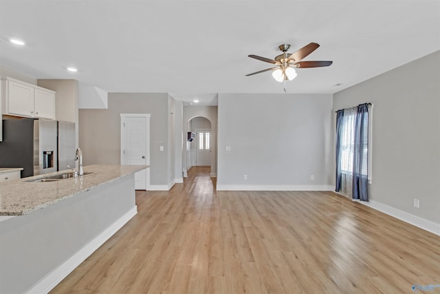 living room featuring arched walkways, baseboards, a ceiling fan, and light wood-style floors
