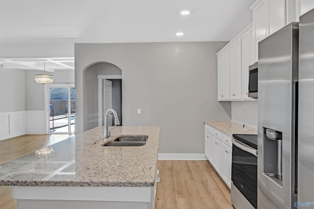 kitchen with a kitchen island with sink, a sink, white cabinetry, light wood-style floors, and appliances with stainless steel finishes