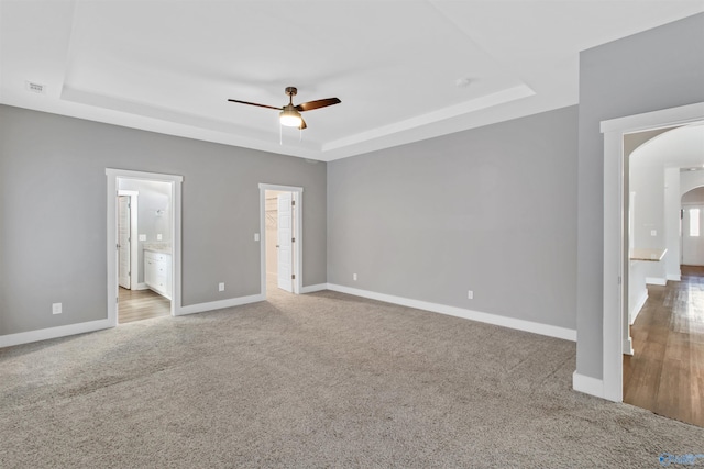 unfurnished bedroom with arched walkways, ensuite bathroom, carpet floors, baseboards, and a tray ceiling