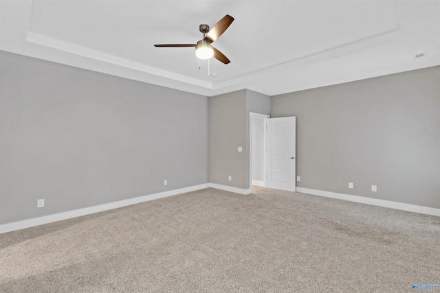 carpeted spare room featuring ceiling fan, a raised ceiling, and baseboards