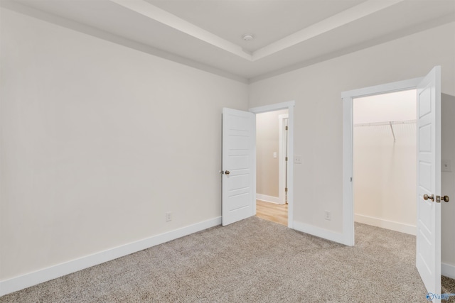 unfurnished bedroom featuring carpet, a closet, a raised ceiling, a spacious closet, and baseboards
