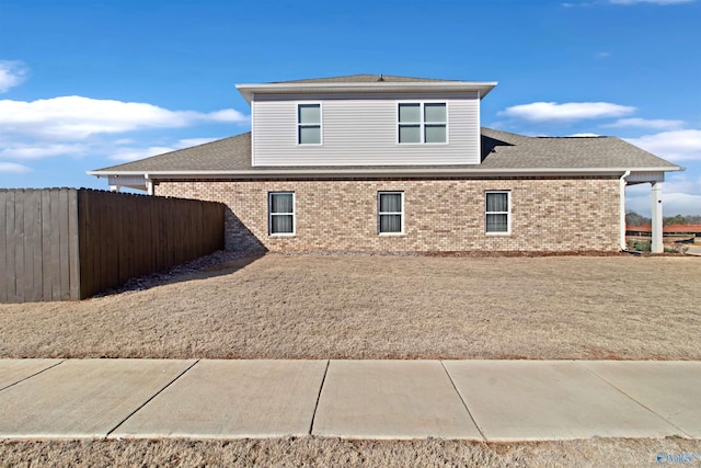 view of side of property with a shingled roof, fence, and brick siding