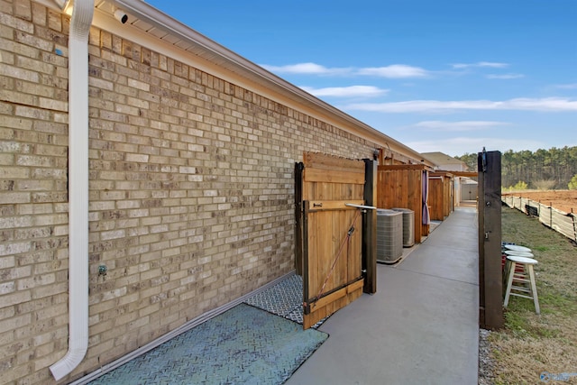 view of side of home featuring brick siding, fence, and central air condition unit