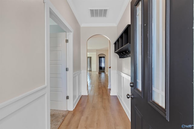 hall with arched walkways, a wainscoted wall, visible vents, ornamental molding, and light wood finished floors