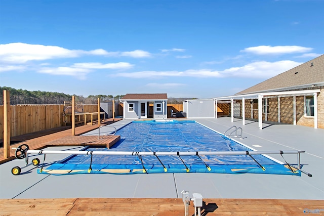 view of pool featuring a deck, a patio, an outdoor structure, fence, and a fenced in pool