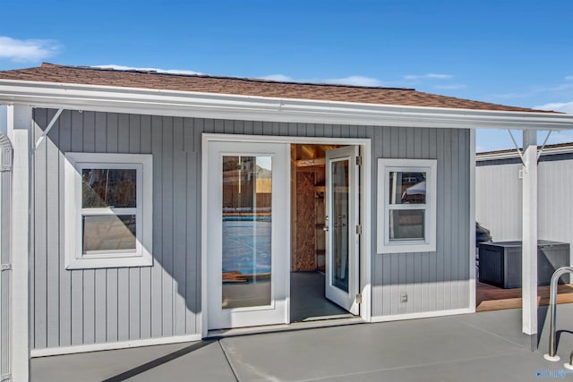entrance to property featuring a shingled roof and a patio