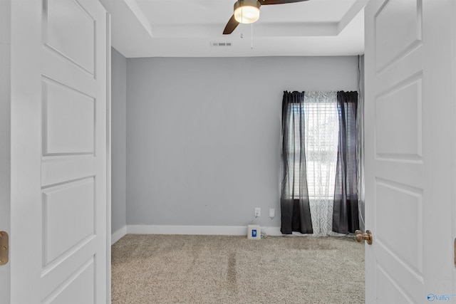 carpeted empty room featuring a raised ceiling, visible vents, ceiling fan, and baseboards