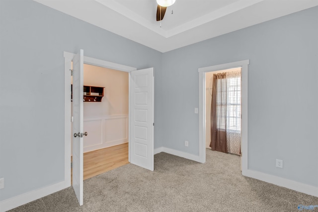 unfurnished bedroom featuring ceiling fan, carpet floors, and a raised ceiling