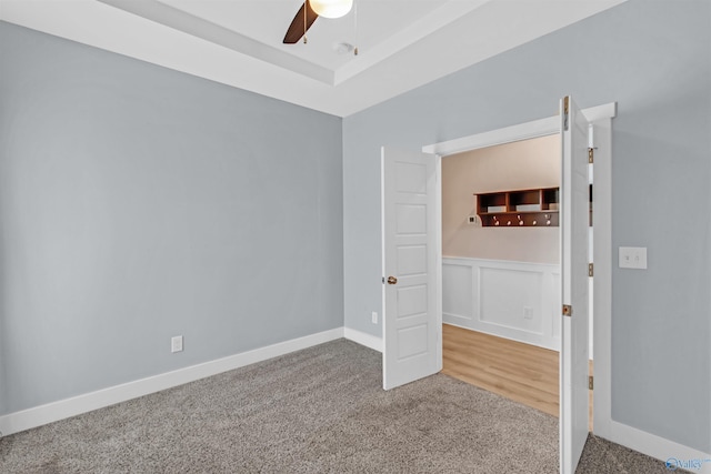 carpeted empty room with a ceiling fan, a tray ceiling, a decorative wall, and baseboards