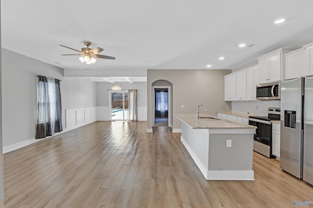 kitchen with a kitchen island with sink, stainless steel appliances, a sink, white cabinets, and light wood-style floors