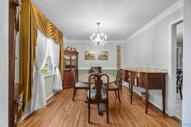 dining space with a notable chandelier, light hardwood / wood-style flooring, crown molding, and a textured ceiling