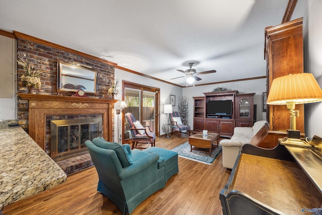 living room with ornamental molding, a fireplace, ceiling fan, and light hardwood / wood-style flooring