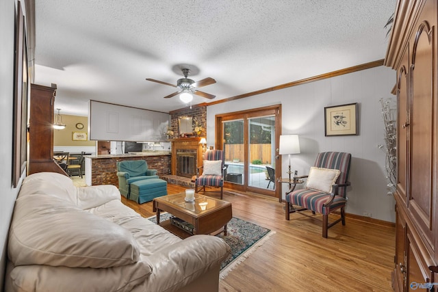 living room featuring ceiling fan, light hardwood / wood-style floors, a fireplace, ornamental molding, and a textured ceiling