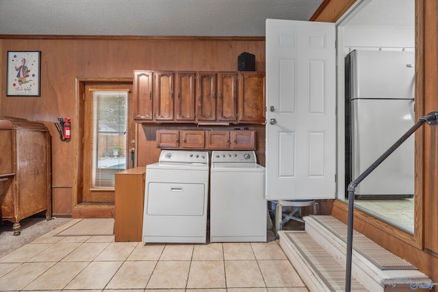 laundry area with wood walls, light tile patterned flooring, cabinets, independent washer and dryer, and a textured ceiling