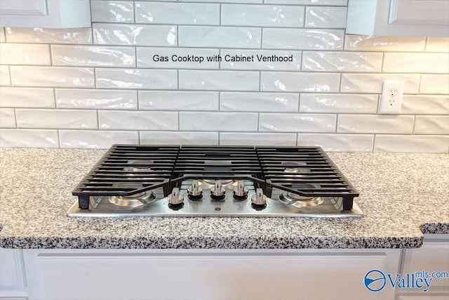 details with stainless steel gas stovetop, light stone countertops, white cabinets, and backsplash