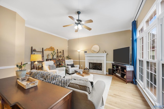 living room featuring a tile fireplace, ceiling fan, light hardwood / wood-style flooring, and crown molding