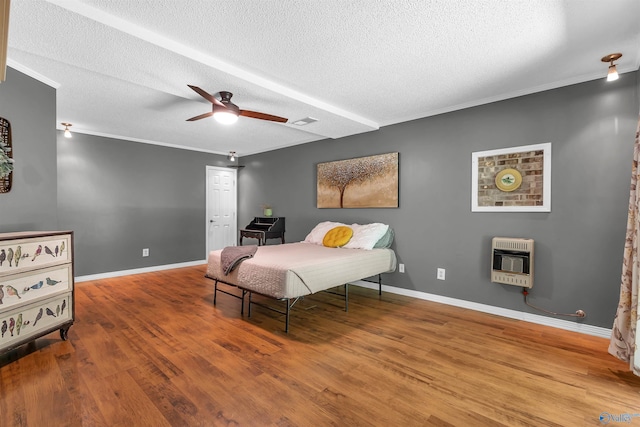 bedroom with baseboards, a textured ceiling, heating unit, and wood finished floors