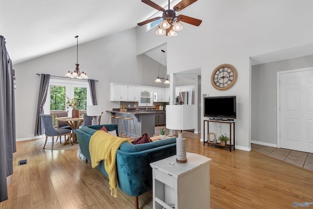 living area with light wood finished floors, high vaulted ceiling, ceiling fan with notable chandelier, baseboards, and visible vents