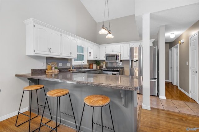 kitchen with a kitchen breakfast bar, appliances with stainless steel finishes, high vaulted ceiling, a peninsula, and white cabinetry