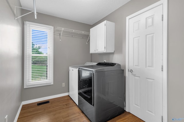 clothes washing area with wood finished floors, baseboards, cabinet space, and washing machine and clothes dryer