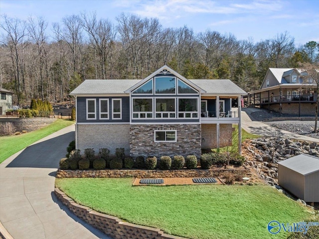 rear view of house featuring stone siding, a lawn, and concrete driveway