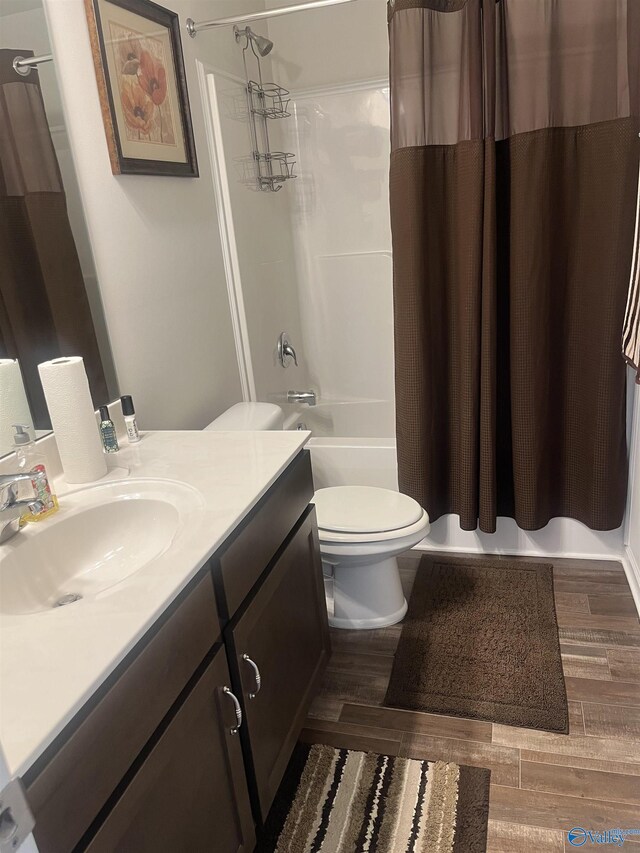 full bathroom featuring wood-type flooring, vanity, shower / bathtub combination with curtain, and toilet