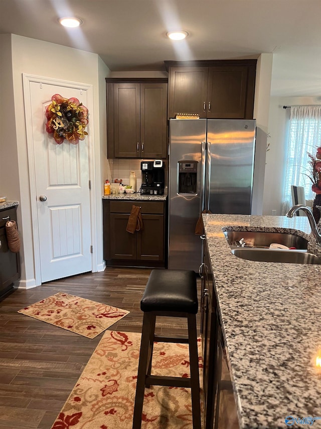 kitchen with sink, dark brown cabinets, light stone countertops, dark hardwood / wood-style floors, and stainless steel refrigerator with ice dispenser