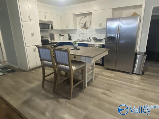 kitchen featuring white cabinets, appliances with stainless steel finishes, sink, backsplash, and light wood-type flooring