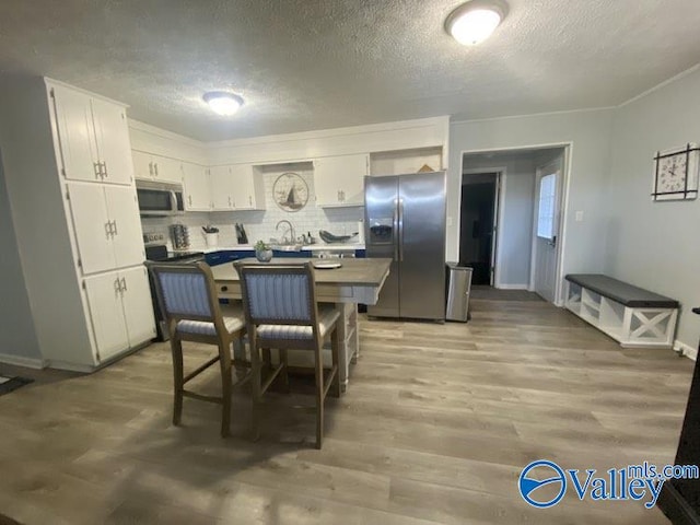 kitchen featuring white cabinetry, stainless steel appliances, tasteful backsplash, a kitchen breakfast bar, and light wood-type flooring