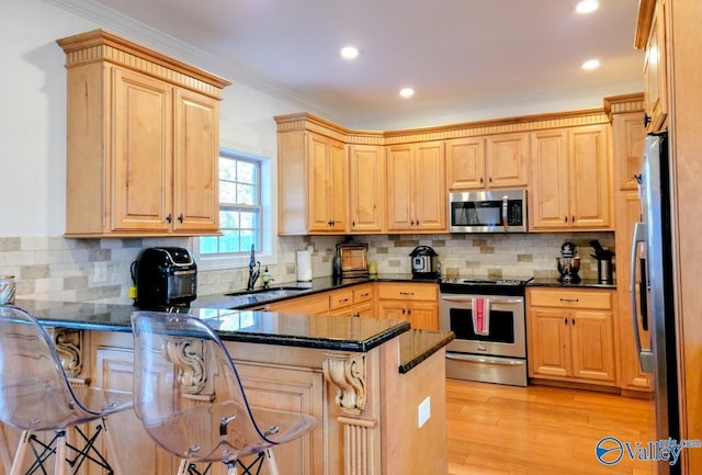 kitchen featuring light brown cabinets, stainless steel appliances, a peninsula, a sink, and light wood finished floors