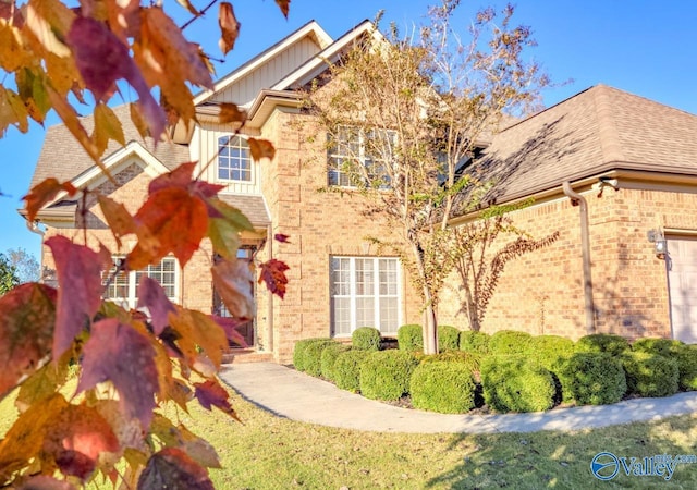 view of front of house featuring an attached garage, a shingled roof, board and batten siding, and brick siding