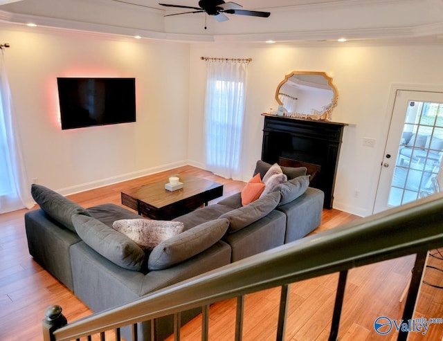 living area with baseboards, a ceiling fan, ornamental molding, wood finished floors, and a fireplace