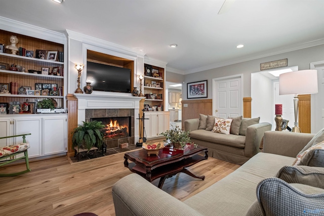 living area featuring built in features, light wood-type flooring, ornamental molding, and a fireplace
