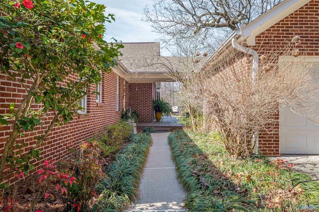 doorway to property featuring a garage, brick siding, and roof with shingles