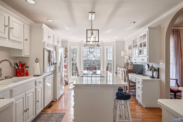 kitchen with a kitchen island, light wood-style flooring, arched walkways, white appliances, and a sink