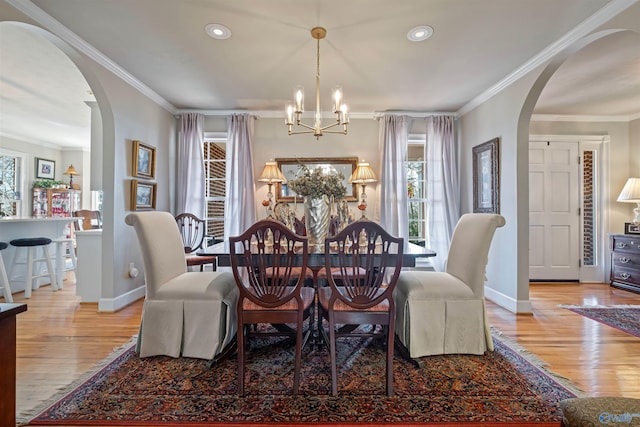 dining room featuring wood finished floors, arched walkways, a notable chandelier, and ornamental molding
