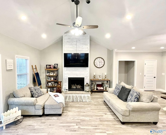 living room featuring ceiling fan, a large fireplace, lofted ceiling, and light hardwood / wood-style flooring