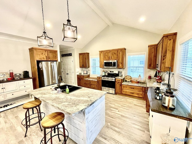 kitchen featuring sink, light stone counters, appliances with stainless steel finishes, pendant lighting, and a kitchen island with sink