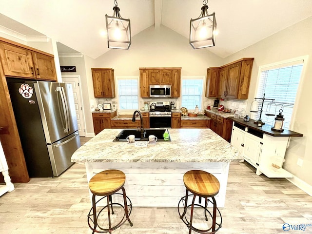 kitchen featuring sink, appliances with stainless steel finishes, decorative light fixtures, and a kitchen island with sink