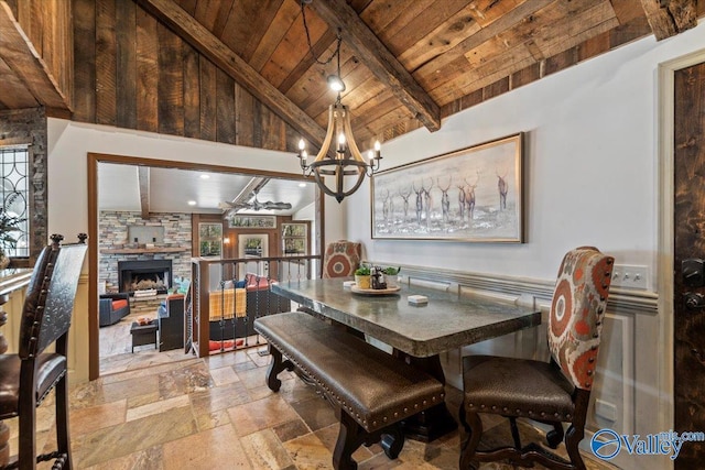 dining room featuring stone tile floors, lofted ceiling with beams, wooden ceiling, a stone fireplace, and a notable chandelier