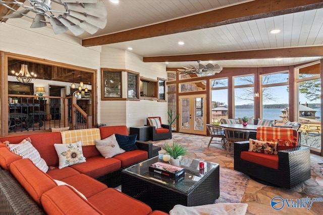 living area with beam ceiling, stone tile flooring, a water view, wood walls, and ceiling fan with notable chandelier